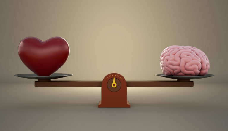 Brain and heart on a wooden balance scale.