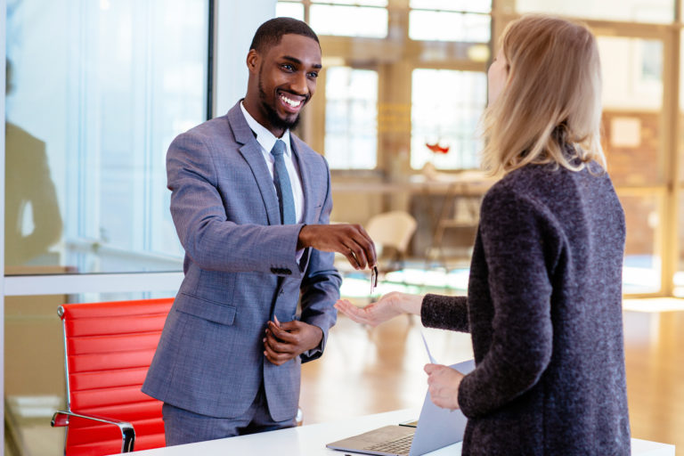 Portrait of a smiling young man in business suit with female client giving her keys to new apartment after signing lease